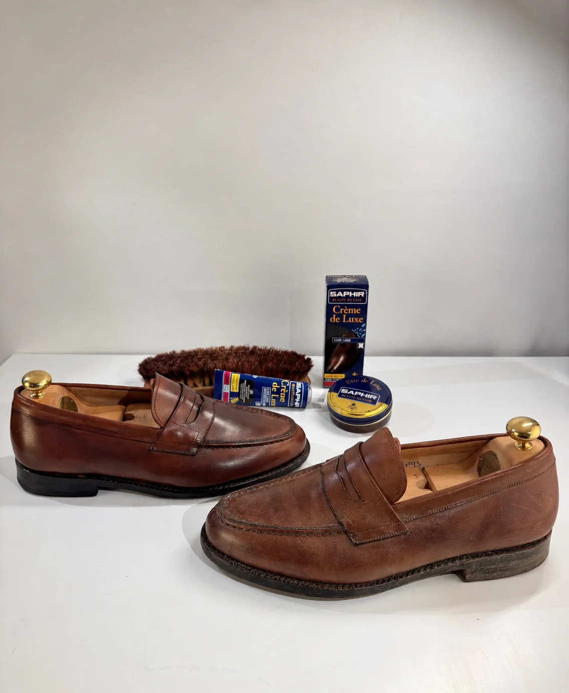 Deux mocassins de cuir brun sur embauchoirs, brosse de crin et produits Saphir posés derrière